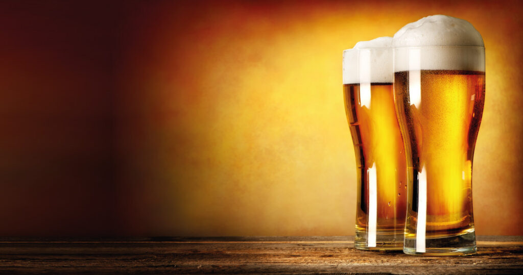 Photograph of two full pint glasses of beer on a wooden table
