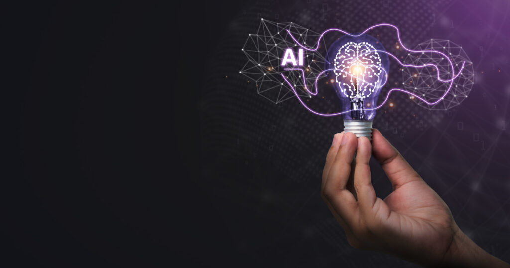 Dark background. Hand holding a lightbulb with the filament shaped like a human brain, glowing purple. Around the bulb, a lilac line of light links networks of nodes, with the letters AI in white.