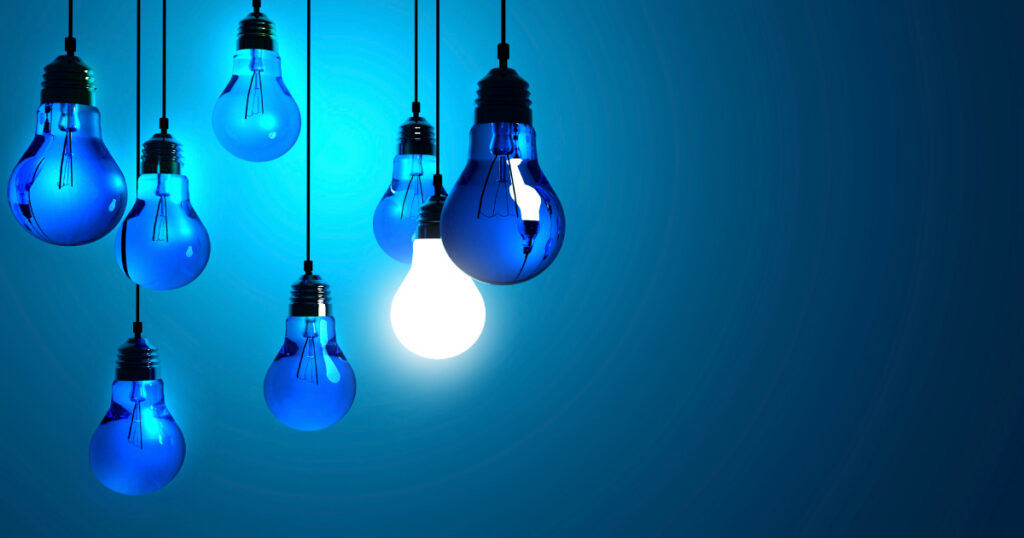 A collection of lightbulbs hanging against a blue background, one of them is switched on
