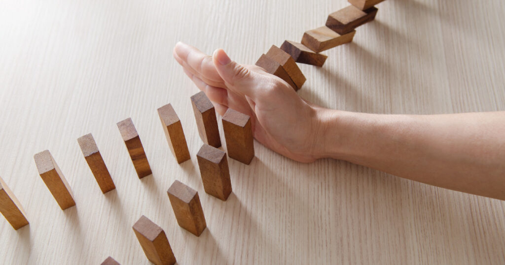 A set of wooden dominos falling and being blocked by a hand, before two upright rows of dominos