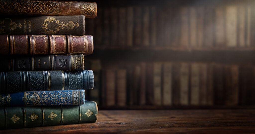 a stack of old books on a table in a library, lit up by a shaft of light