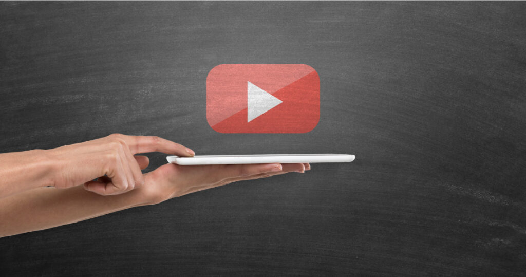 Someone pressing their finger against a mobile phone they are holding flat on their other hand. Above the phone is a video play symbol